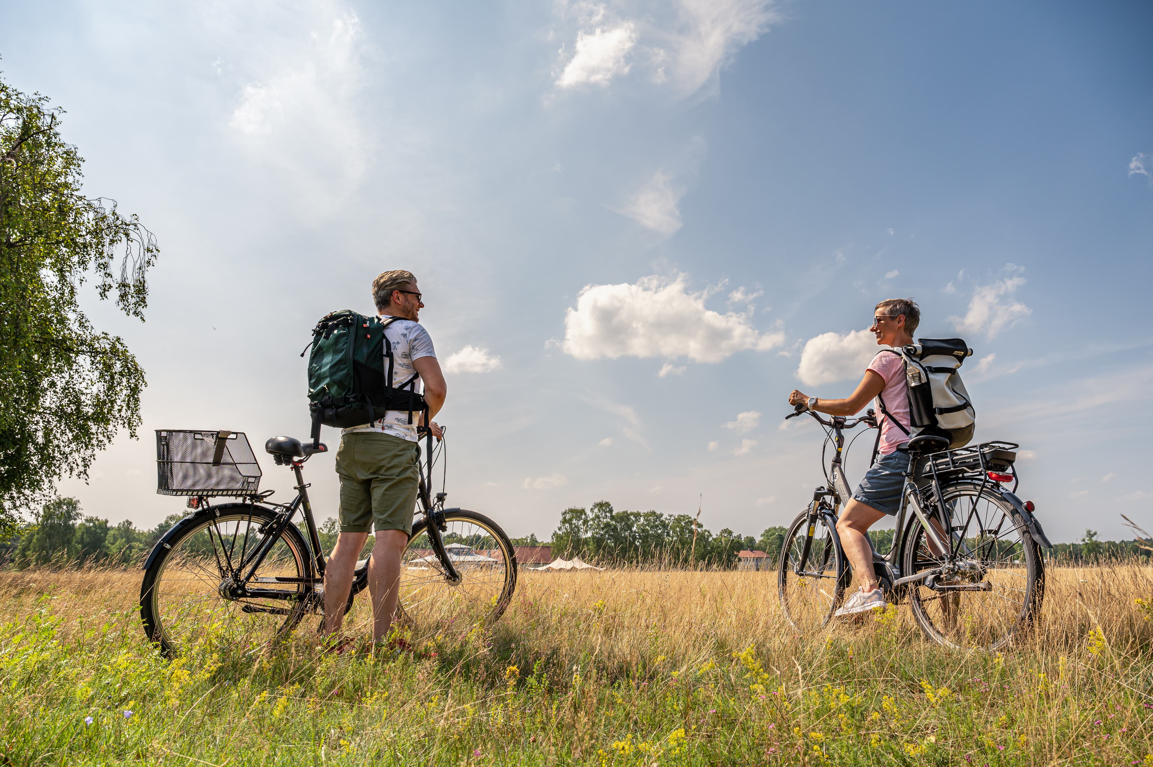 Ein Paar mit Fahrrädern steht auf einer sonnigen Sommerwiese und sieht sich an.