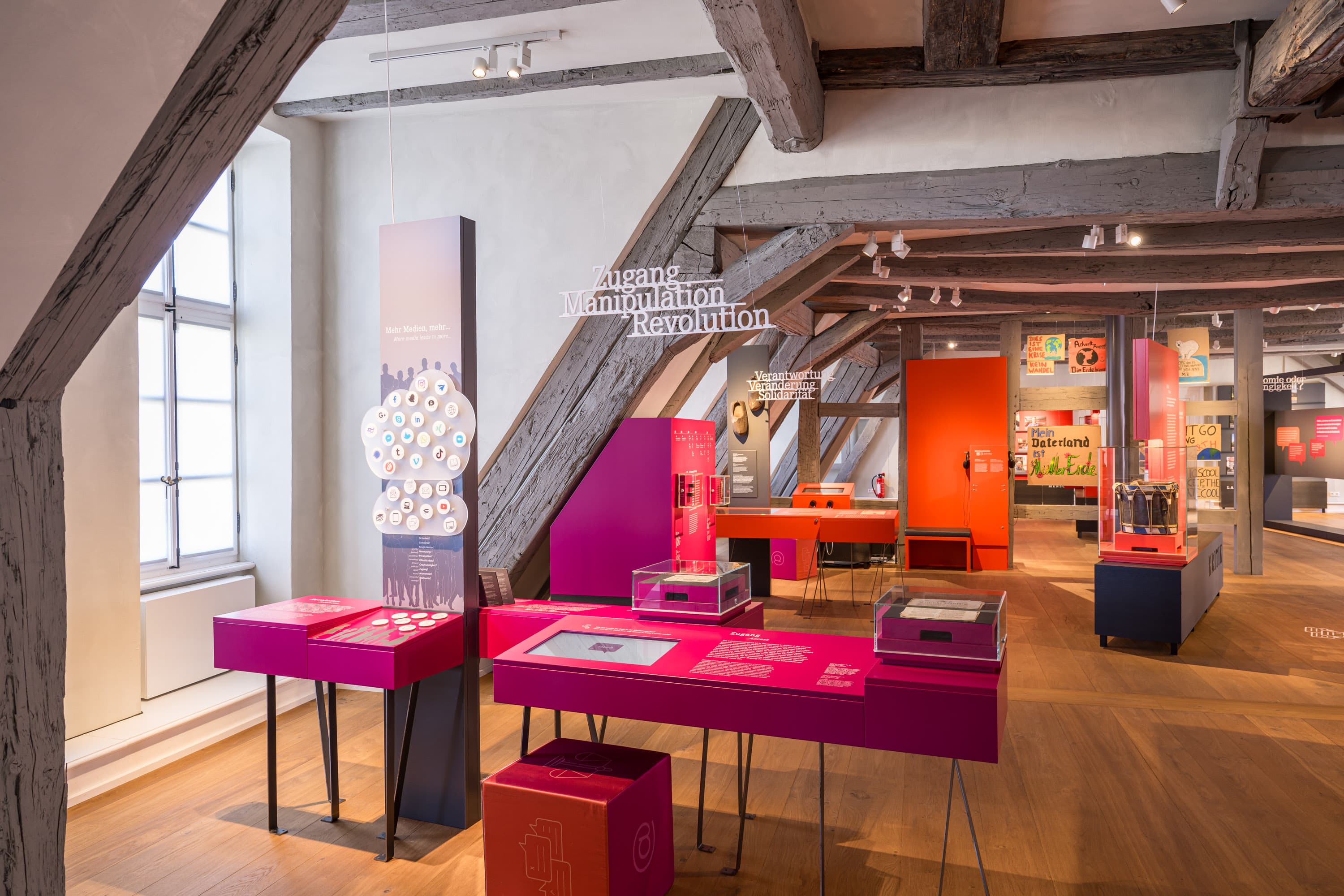 moderner Ausstellungsraum im Residenzmuseum Celle mit farbigen Exponaten unter rustikalen Holzbalken.