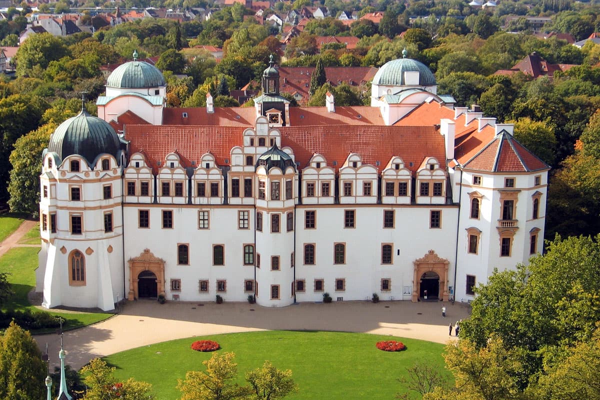 Das weiße Celler Schloss und Residenzmuseum mit seinen roten Dächern und Türmen, umgeben von einer Parkanlage.