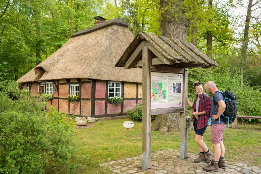 Das Bild zeigt zwei Wanderer die sich eine Infotafel vor dem Hexenhaus in Wesel anschauen.